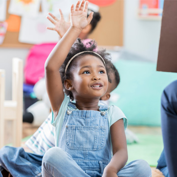 little girl sitting on floor with her hand raised